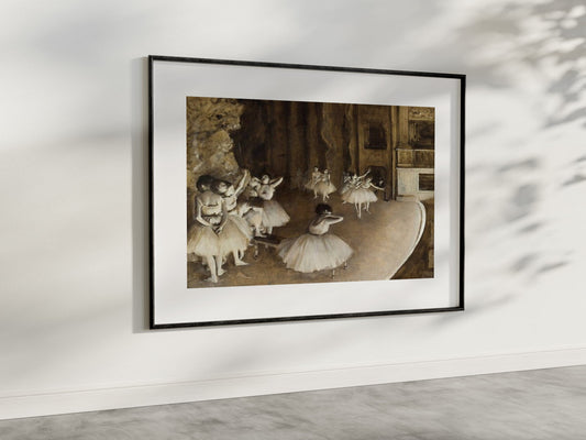 A refined presentation of "The Ballet Rehearsal on Stage" by Edgar Degas, framed and hung in a modern, well-lit room. The painting captures the essence of a ballet rehearsal with its detailed depiction of ballerinas in various poses, using a palette of warm, earthy tones. This art reproduction brings a timeless charm and artistic flair to your living space, perfect for those who appreciate fine art and ballet.