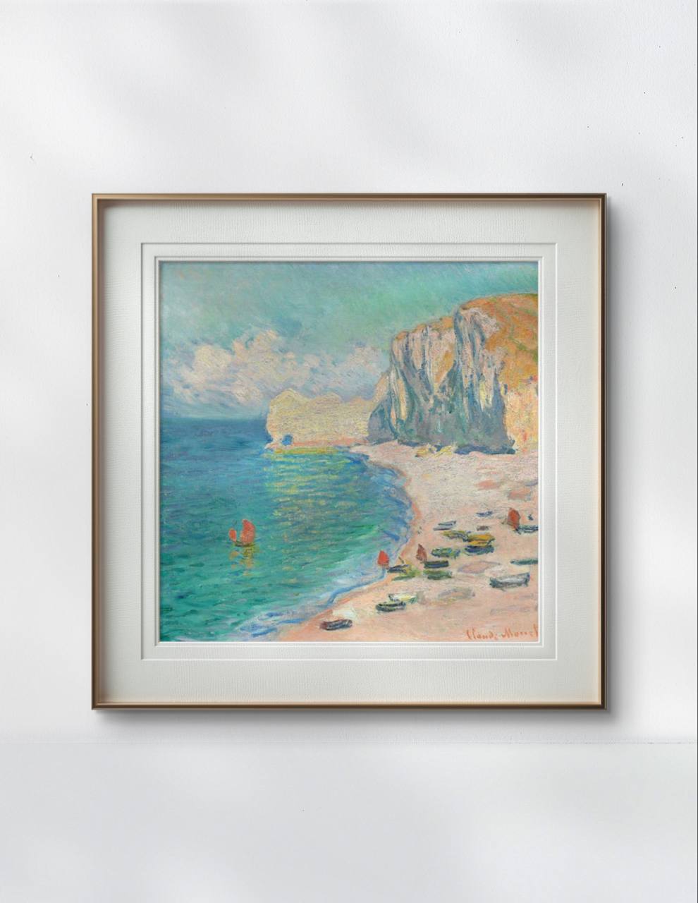 The same framed Monet painting is displayed on a light-colored wall, highlighting the pastel tones of the sea, sand, and sky. The simple yet elegant frame allows the artwork to be the main focus.
