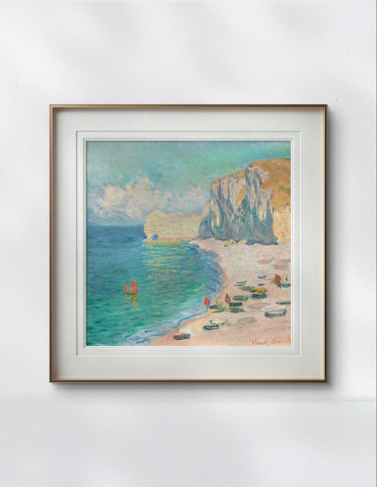 The same framed Monet painting is displayed on a light-colored wall, highlighting the pastel tones of the sea, sand, and sky. The simple yet elegant frame allows the artwork to be the main focus.