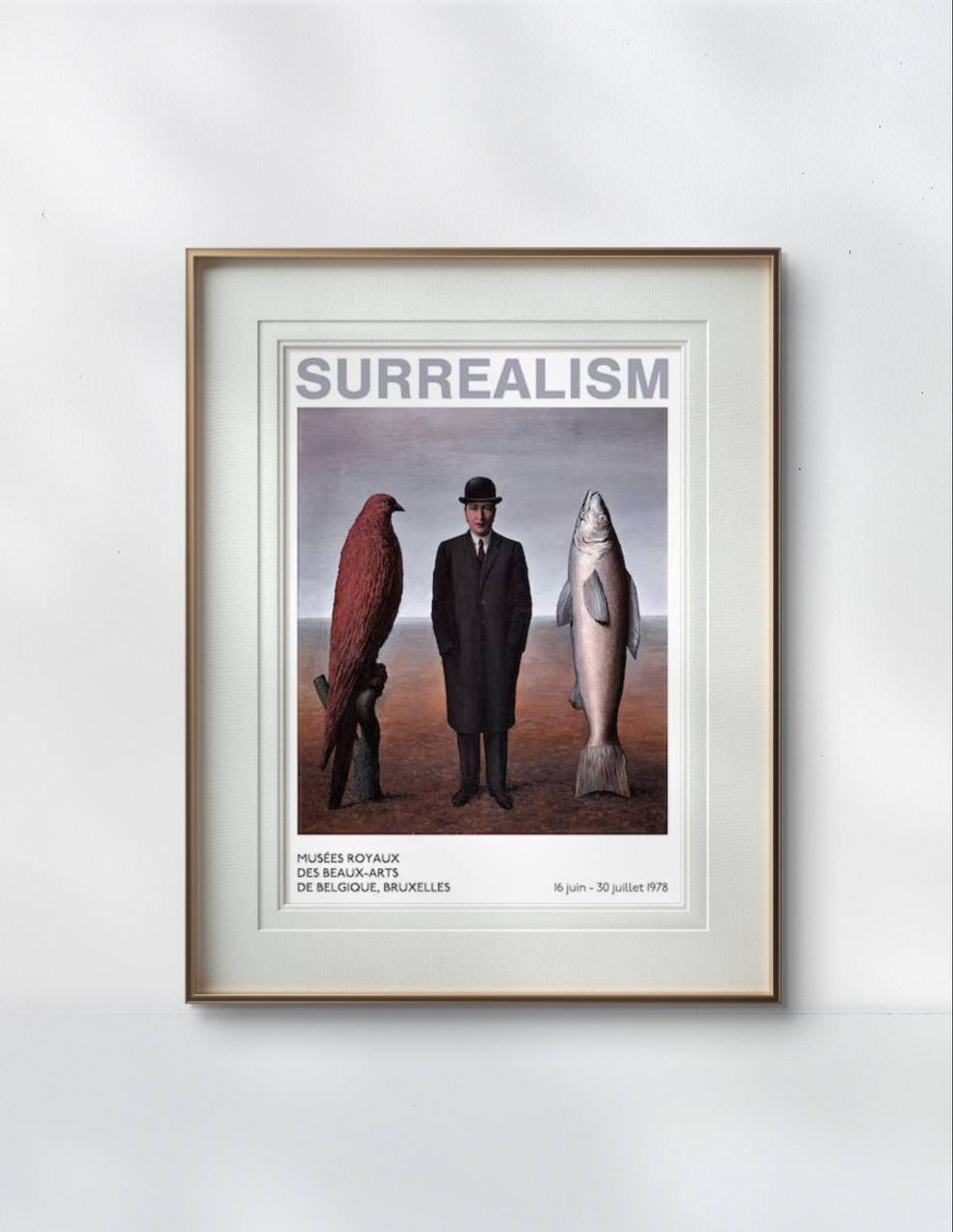 The framed poster shows a man in a suit standing between a bird and a fish. The word 'Surrealism' is at the top. The frame has a simple, elegant design, displayed on a plain wall