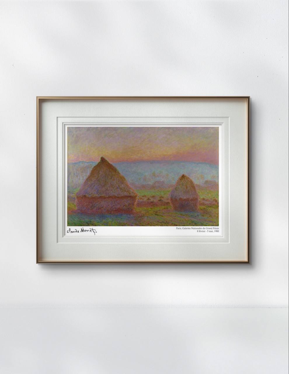 A framed Monet print of haystacks at sunset. The soft pink and orange sky contrasts with the earthy tones of the haystacks. The simple frame highlights the serene artwork