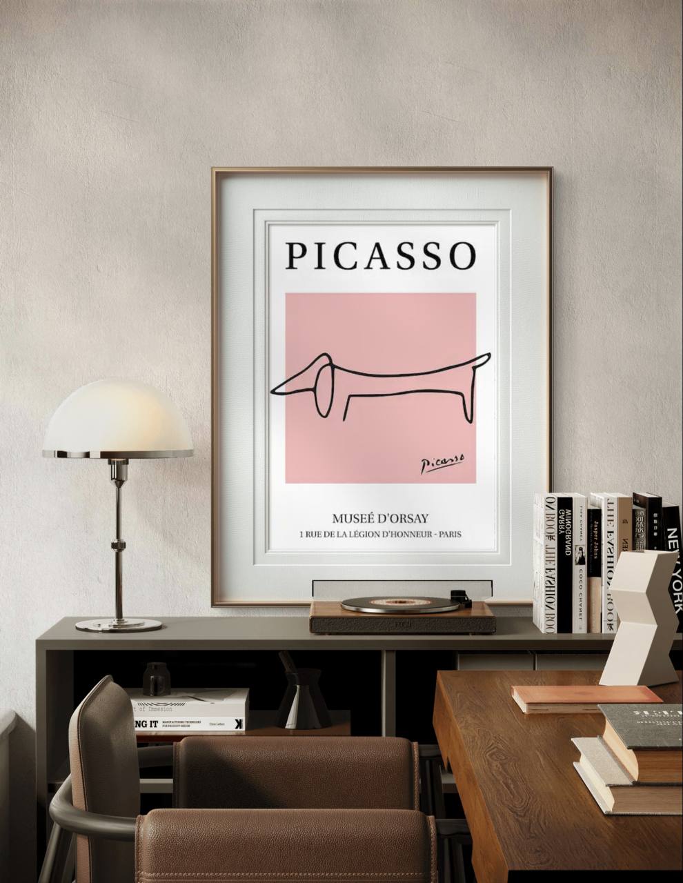 A framed poster featuring a simple line drawing of a dachshund by Picasso, displayed in a modern room. The light-colored frame complements the soft pink background
