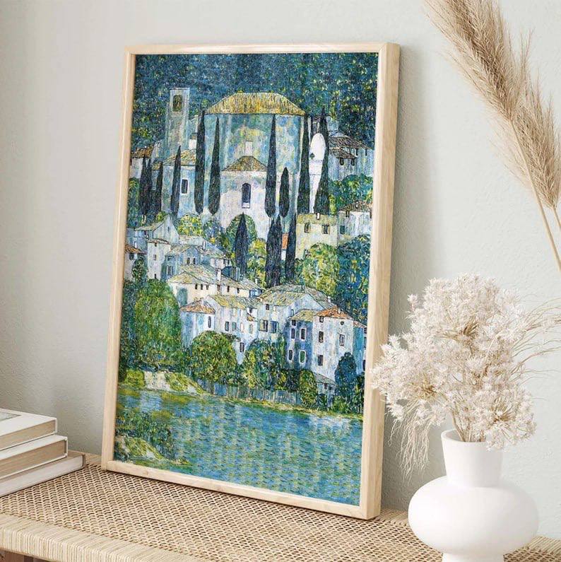 A framed painting of Cassone with its prominent church and cypress trees, placed on a natural wooden shelf. The artwork’s peaceful landscape contrasts with the minimal decor, bringing a touch of serenity to the space.