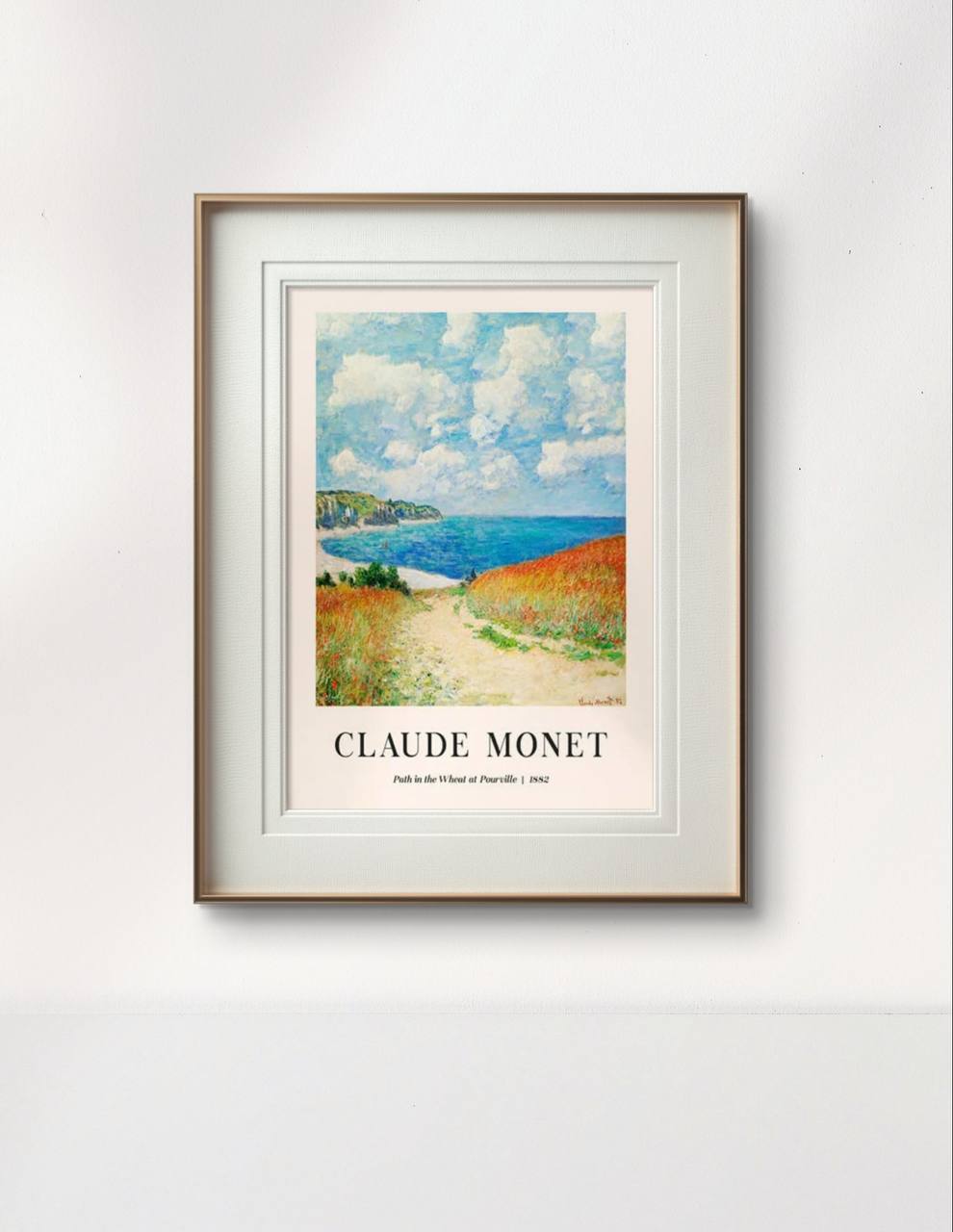 The same wheat field painting is framed in a simple wooden frame with white matting. The path, sea, and clouds give a peaceful and open feeling to the composition, set against a light wall.