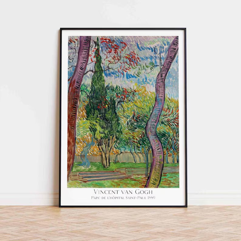 The second image displays the same Van Gogh poster, this time mounted on a plain white wall. The frame has a minimalist design with a thin wooden border, complementing the simple yet sophisticated decor of the room. The room is bathed in natural light, which highlights the vibrant colors of the poster. The artwork depicts a lush garden scene with a mix of trees and shrubs in full bloom, characteristic of Van Gogh's energetic style. The setting includes a modern white vase and a beige armchair, creating a ha