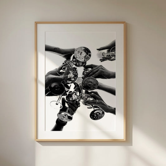 A black and white photograph capturing a celebratory moment, featuring multiple hands raising and clinking champagne glasses from a top-down perspective. The reflections on the glass create a dynamic and elegant visual effect, symbolizing joy, luxury, and togetherness. The monochrome aesthetic adds a timeless and sophisticated feel.