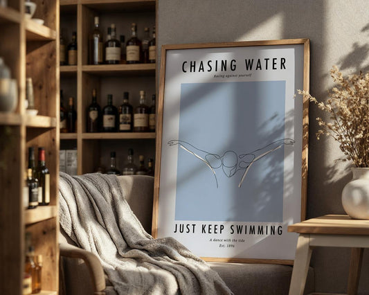 Framed poster with 'Chasing Water, Just Keep Swimming' text in a cozy room with a bookshelf and chair.
