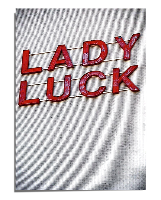 A white textured background featuring the words "Lady Luck" in three-dimensional red letters, connected by thin gold wires, creating a vintage and elegant visual effect.