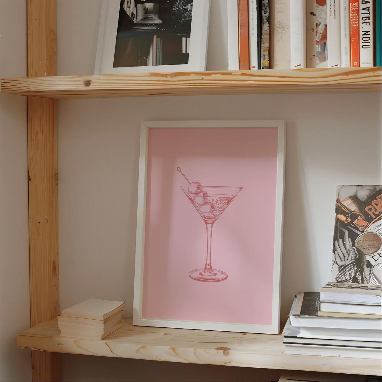 Wooden shelf with books and a framed picture of a cocktail on a pink background.