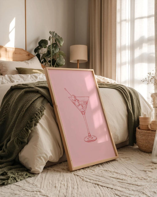 Framed pink print of a cocktail glass on a bed in a cozy bedroom.