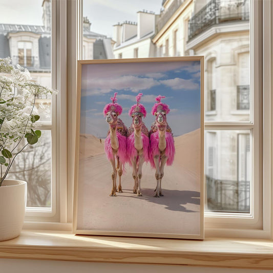 Three camels are walking side by side through a sandy desert. Each camel is dressed in bright pink feathers and detailed accessories, with matching pink headpieces. The sky above is clear with light clouds, creating a vivid contrast against the beige dunes and flamboyant outfits.
