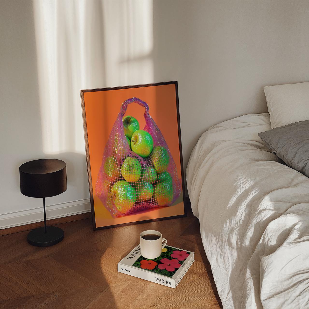 Framed artwork of apples in a net bag on a wooden floor next to a bed.