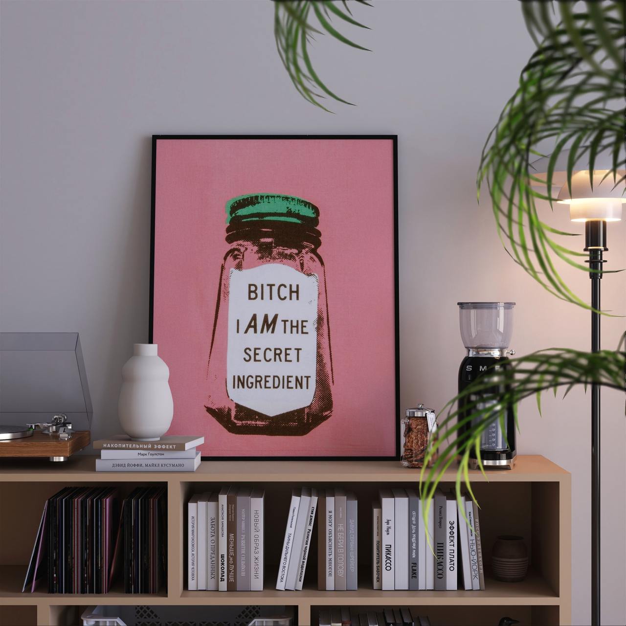 Framed artwork with a pink background and text on a shelf with books and decor items.