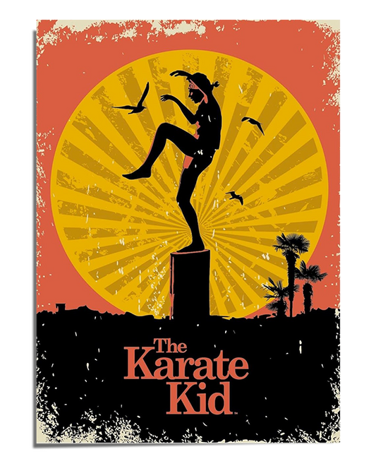 A vintage-style movie poster featuring the silhouette of Daniel LaRusso performing the famous crane kick on a wooden pillar, inspired by The Karate Kid. The background consists of a large, glowing yellow sun with radiating lines, set against a red-orange sky with distressed textures for a retro effect. Several birds fly across the scene, adding movement. Below, dark silhouettes of palm trees and rooftops complete the sunset setting. The title "The Karate Kid" appears in bold, classic typography at the botto