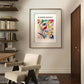 A modern interior setting with a beige chair and an abstract design rug in the foreground. The same poster of the painting "Composition in Red, Blue, Green, and Yellow" by Kandinsky is framed and well-lit on the wall. To the left, there are shelves with books and decorative objects. This wall art poster is ideal for home decor, enhancing any room with vibrant modern art.