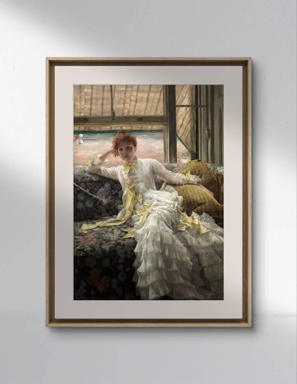 A minimalist interior setting with a white wall and wooden flooring. The framed poster of "Seaside, July" by James Tissot is hung on the wall, illuminated by natural light. The painting reproduction serves as excellent wall art for a home gallery wall or a serene reading nook, bringing a touch of Victorian elegance to the decor.