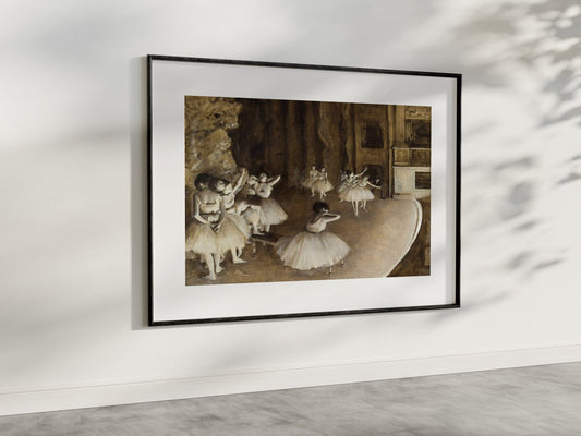 A refined presentation of "The Ballet Rehearsal on Stage" by Edgar Degas, framed and hung in a modern, well-lit room. The painting captures the essence of a ballet rehearsal with its detailed depiction of ballerinas in various poses, using a palette of warm, earthy tones. This art reproduction brings a timeless charm and artistic flair to your living space, perfect for those who appreciate fine art and ballet. 