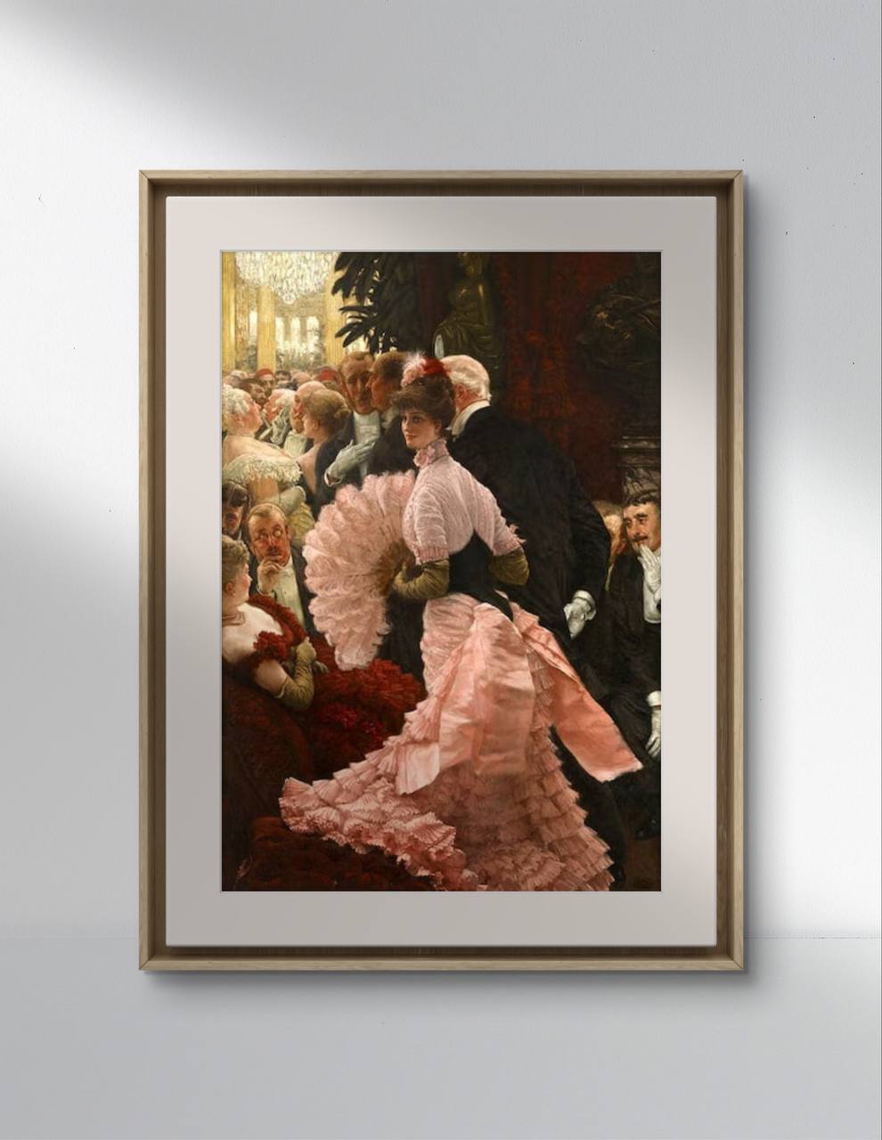 A poster of "A Political Woman" by James Tissot displayed on a minimalist white wall. The artwork features a woman in a pink dress with a fan, surrounded by a lively crowd at a sophisticated event.   This art reproduction brings a classic and elegant touch to your home decor. Keywords: Wall Art, home decor, painting, art reproduction, famous artist, Poster, print, James Tissot, A Political Woman.