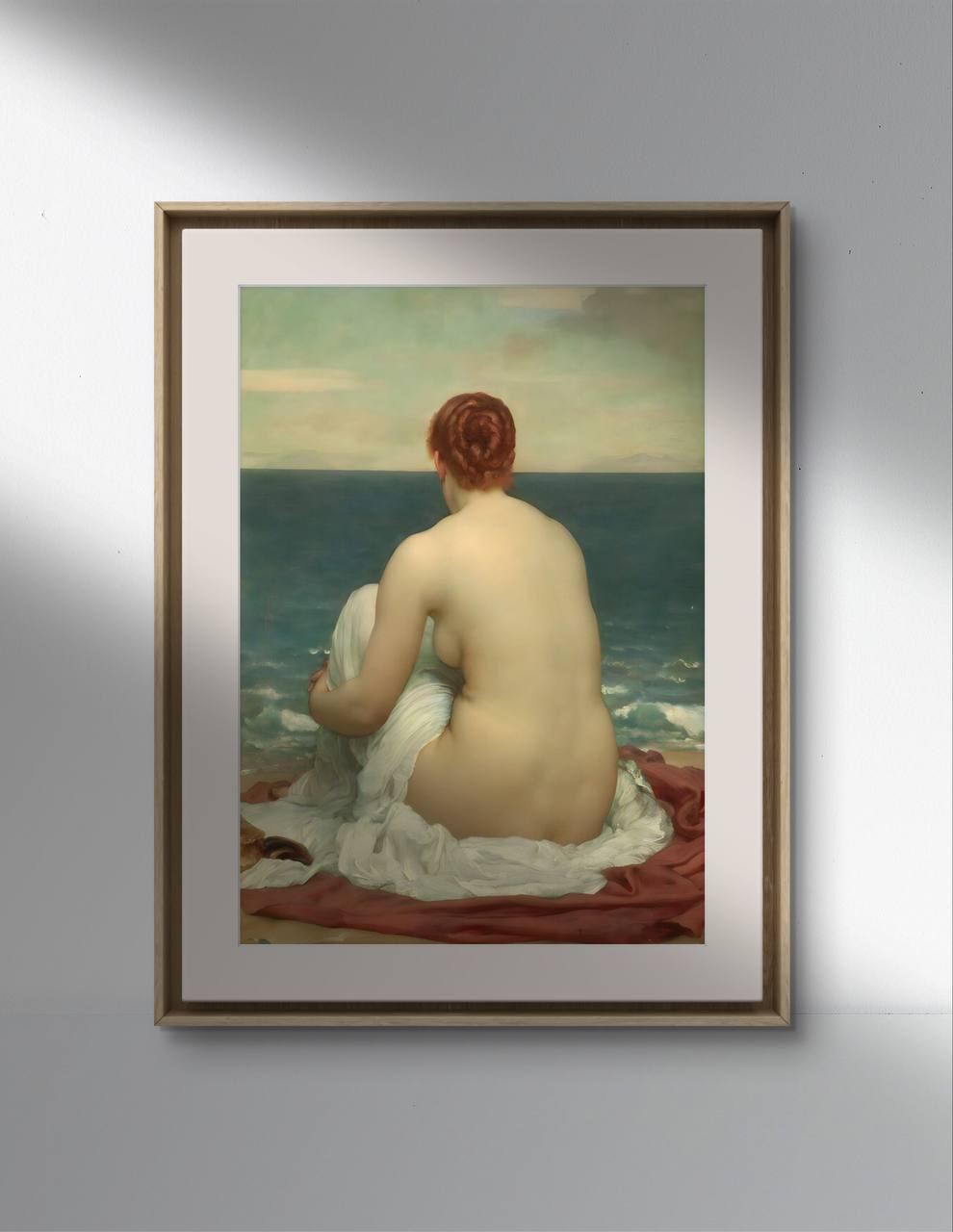The second image shows the same poster of "Psamathe" by Frederick Leighton in a minimalist frame with a golden edge, hung on a gray wall above a dark wooden cabinet. The cabinet holds antique books and a modern sculpture, blending classic and contemporary elements. The painting's serene beach scene adds a calming atmosphere to the room.
