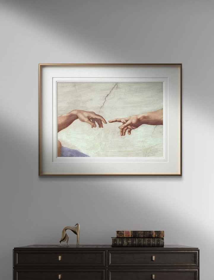 The third image features the "The Creation of Adam" hands poster by Michelangelo, framed and displayed above a dark wooden cabinet. The classic frame complements the detailed artwork, creating a sophisticated and timeless look. The iconic image of the almost-touching hands brings a touch of Renaissance art to the modern decor setup