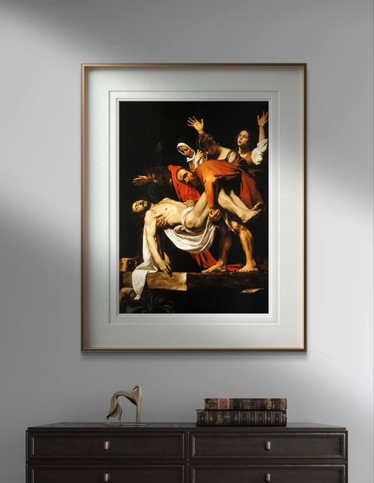 The first image shows a framed poster of Caravaggio's "The Deposition of Christ" on a gray wall. The framed poster features a simple golden border, enhancing the dramatic depiction of Christ being lowered from the cross. Below this classical art reproduction, there's a dark wooden table with antique books and a modern decorative sculpture, adding a touch of elegance to the wall decor.