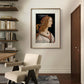 A framed Renaissance portrait hangs in a minimalist room. A beige chair sits in front of a wooden desk with shelves on the left. The detailed artwork contrasts beautifully with the modern, simple decor.