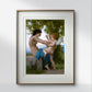 The painting of the woman and Eros is framed with a white and gold frame, hanging on a minimalist white wall. The soft colors of the artwork stand out against the clean, simple background.