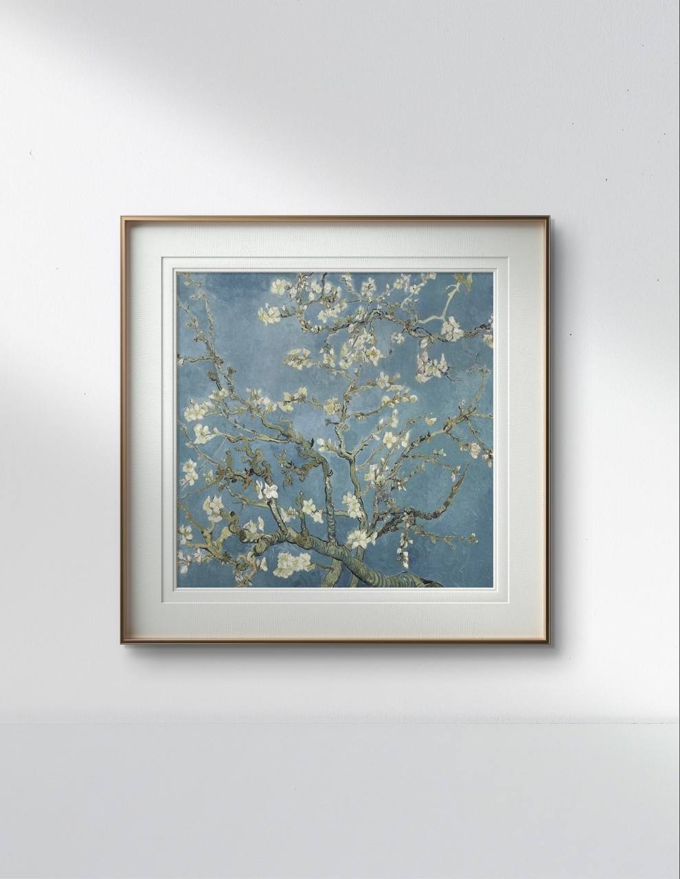 The framed reproduction of Van Gogh's "Almond Blossom" hangs on a minimalist white wall. The white and gold frame accentuates the soft blues and whites of the artwork, adding a peaceful touch to the room.