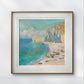 The same framed Monet painting is displayed on a light-colored wall, highlighting the pastel tones of the sea, sand, and sky. The simple yet elegant frame allows the artwork to be the main focus.