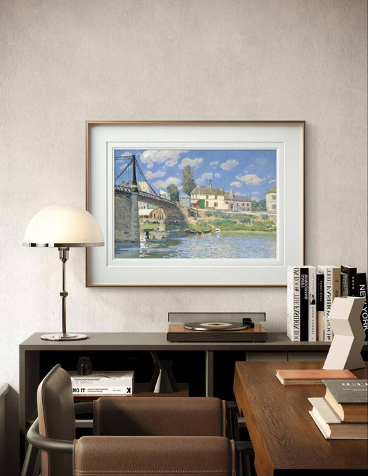 Framed impressionist painting of a river and bridge, hanging in a cozy home office. The serene scene of boats and houses bathed in sunlight adds a calming, picturesque touch to the room.