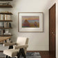 A framed Monet painting of haystacks hangs in a modern room. The neutral decor and the elegant armchair complement the warm tones of the sunset in the artwork