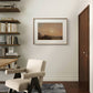 A framed painting of a serene landscape by John Constable hangs on a neutral-colored wall. The soft colors of the sunset over the hills bring a calming atmosphere to the room