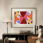 A framed abstract print with bright geometric shapes in red, pink, and orange. The bold colors and dynamic design bring energy and modern style to the room's neutral decor.