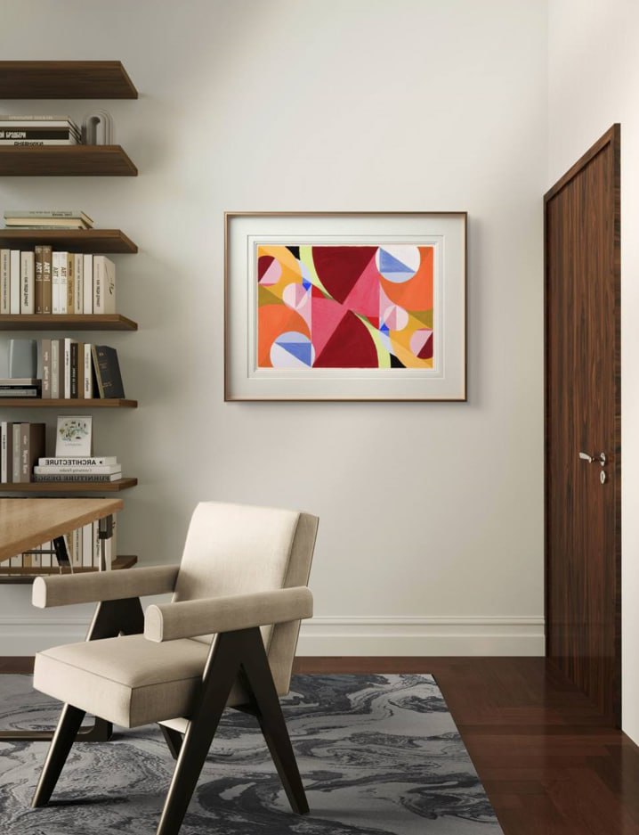 A framed abstract artwork with vibrant overlapping shapes hangs in a minimalist office space. The geometric design contrasts elegantly with the simple, modern furniture