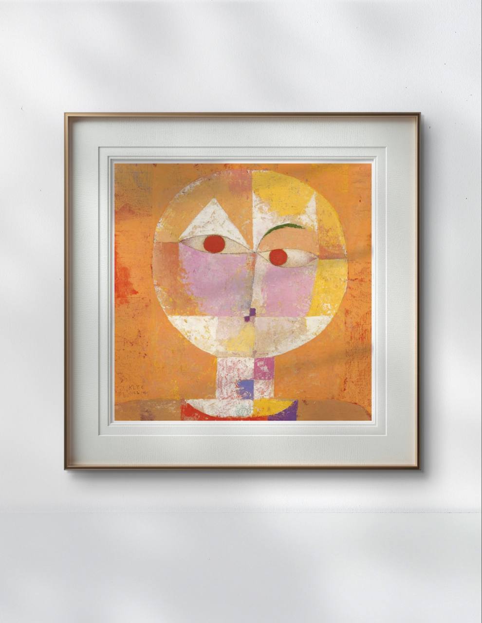 A framed print of 'Senecio' by Paul Klee hangs in a minimalist office. The geometric face in shades of orange and pink creates a striking contrast with the clean lines of the room's design