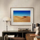  A framed sand dunes poster hangs above a desk in a stylish study. The space features a turntable, books, and a lamp, offering a warm and sophisticated atmosphere.