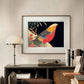The framed "Golden Pheasant in the Snow" artwork hangs on a minimalist white wall, its bold colors and intricate details creating a striking focal point in the modern space.