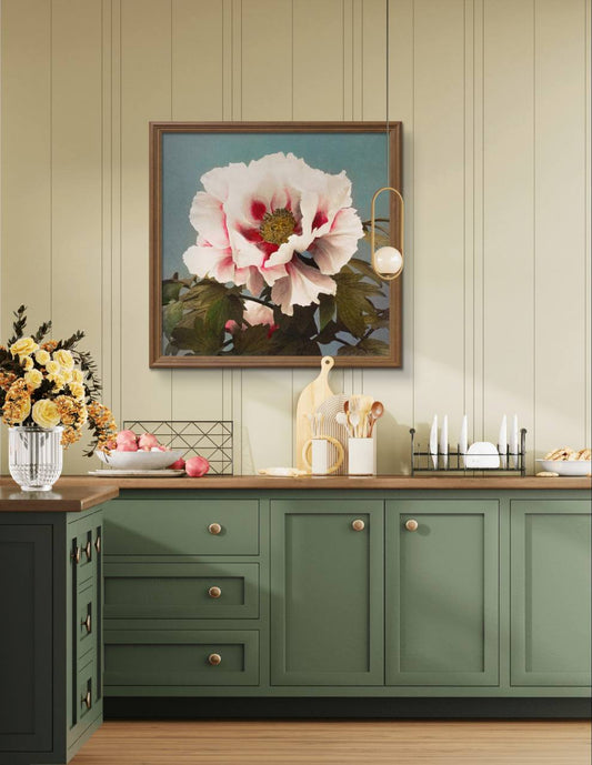 The same framed pink peony artwork is shown hanging on a light green kitchen wall. Below it is a wooden countertop with kitchen decor, including a vase of flowers, cutting boards, and plates, blending modern design with floral elegance.