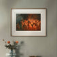 The framed painting of nymphs dancing around a bonfire is displayed in a modern room, hung above a wooden cabinet with flowers. The warm tones of the painting's flames add a dramatic touch to the neutral, minimalist decor.