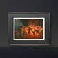 The framed artwork is showcased in a dark, modern room. The bonfire’s warm glow contrasts with the black wall, emphasizing the ethereal dance of the nymphs in the painting’s vibrant, fiery hues.