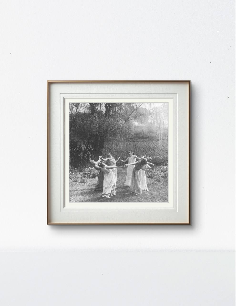 The framed vintage photograph of women dancing in a circle is displayed in a modern room. The monochromatic tones contrast with the clean and minimalistic decor, adding a touch of timeless elegance to the space