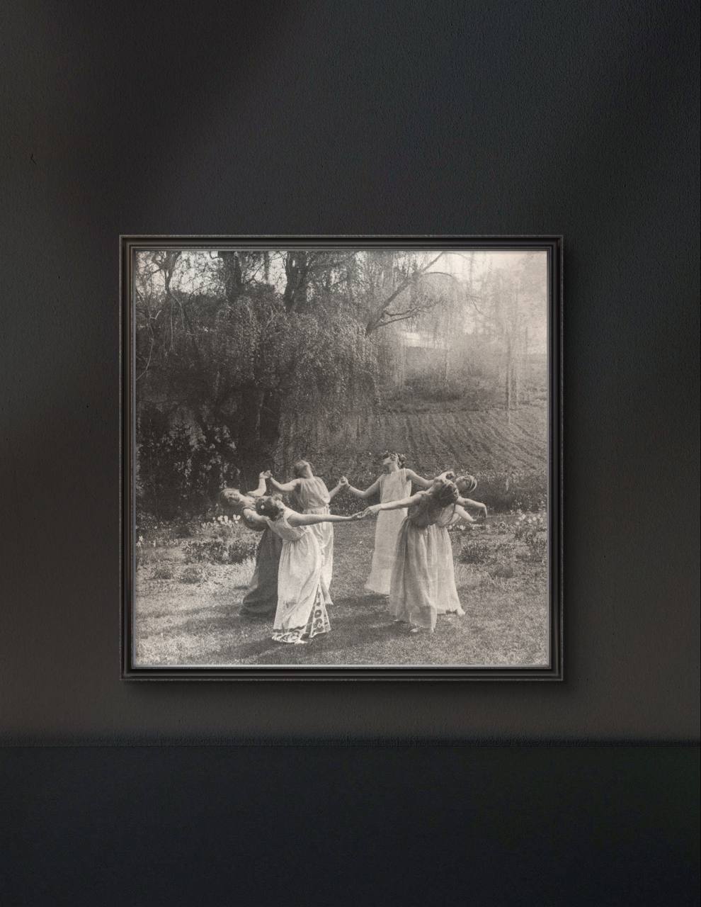 The framed artwork, set against a dark wall, enhances the ethereal quality of the vintage photograph. The contrast between the light dancers and the dark background creates a sense of mystery and enchantment.