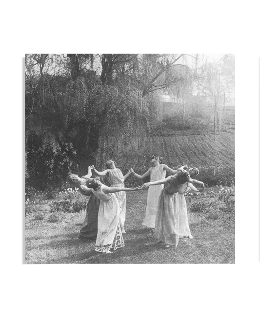  A vintage black-and-white photograph of women in flowing dresses dancing in a circle in a grassy field. Their graceful movements and serene surroundings evoke a sense of harmony with nature, reminiscent of a ritualistic gathering.