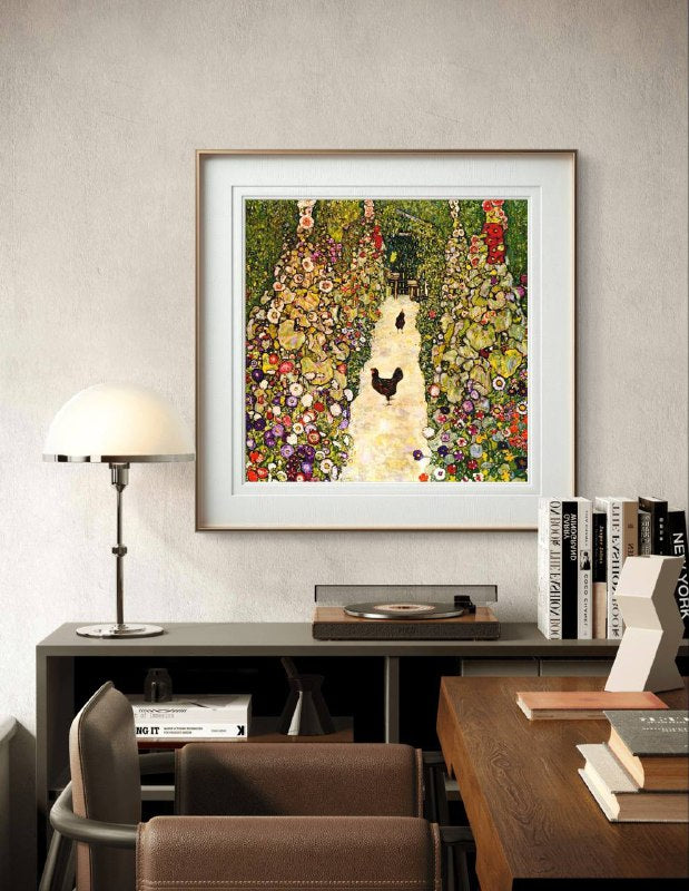 A framed painting of a garden path with chickens, displayed above a modern desk with books and a record player. The bright flowers and greenery in the artwork add a lively contrast to the simple, neutral decor of the room.