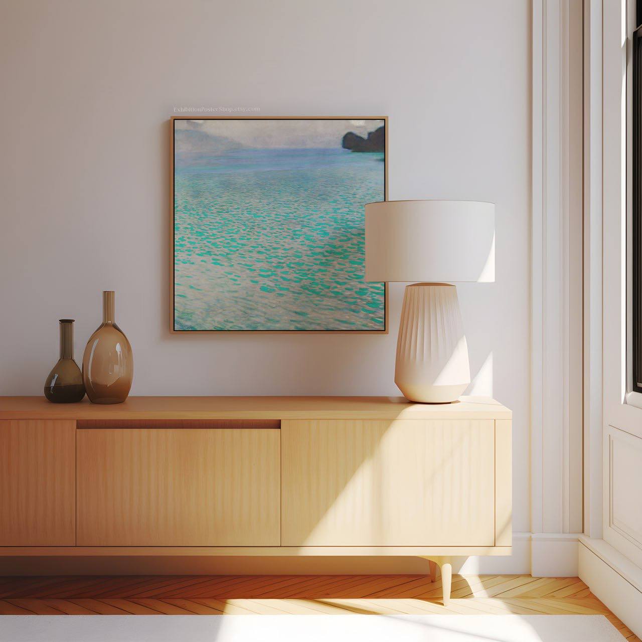 A framed painting of Lake Attersee in a modern room, hanging above a light wooden sideboard with simple decor. The vibrant turquoise water contrasts with the muted tones of the room, creating a relaxing and natural atmosphere.