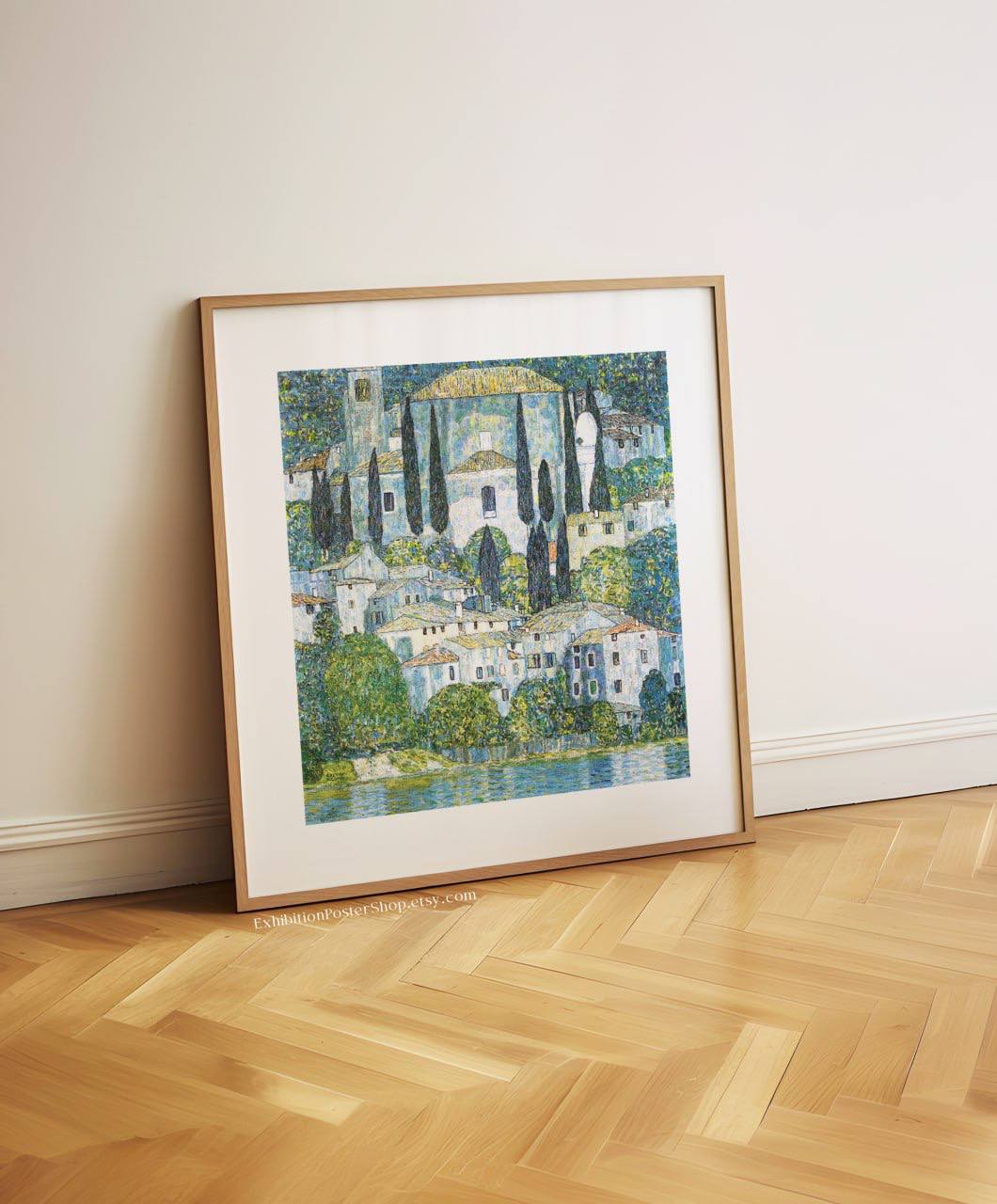 A framed painting of the serene town of Cassone, leaning against a white wall. The detailed church and surrounding houses are painted in soft blues and greens, adding a tranquil, coastal feel to the room.