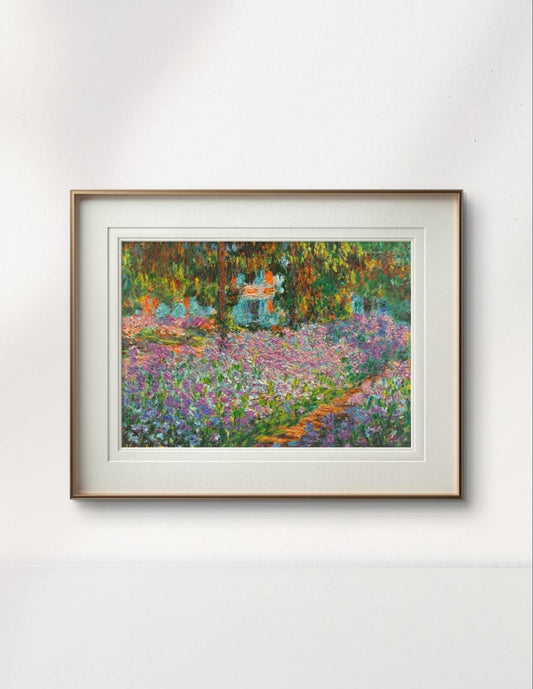 The same garden painting of purple irises framed in a simple wooden frame with white matting. The bright flowers and greenery contrast against the light-colored wall, giving the piece a peaceful, inviting look.