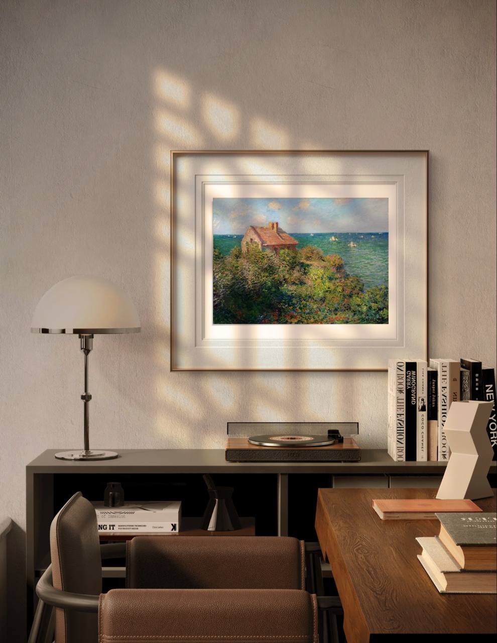 The framed artwork is displayed in a modern room, above a desk with books and a lamp. Sunlight filters through, casting soft shadows, and highlighting the serene coastal painting.