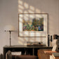 The framed artwork, labeled “Claude Monet – A Corner in the Garden at Montgeron,” is displayed above a desk with a lamp and books. The natural light highlights the peaceful and vibrant garden scene.