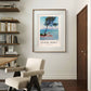The framed painting is displayed in a minimalist room with modern furniture and bookshelves. Soft sunlight shines on the artwork, enhancing the calm blues of the sea and sky.